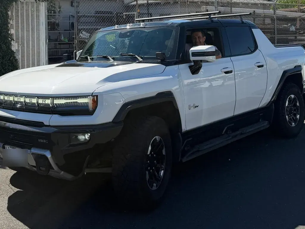 White GMC HUMMER EV pickup with the PG Auto Glass owner seated at the open driver's window