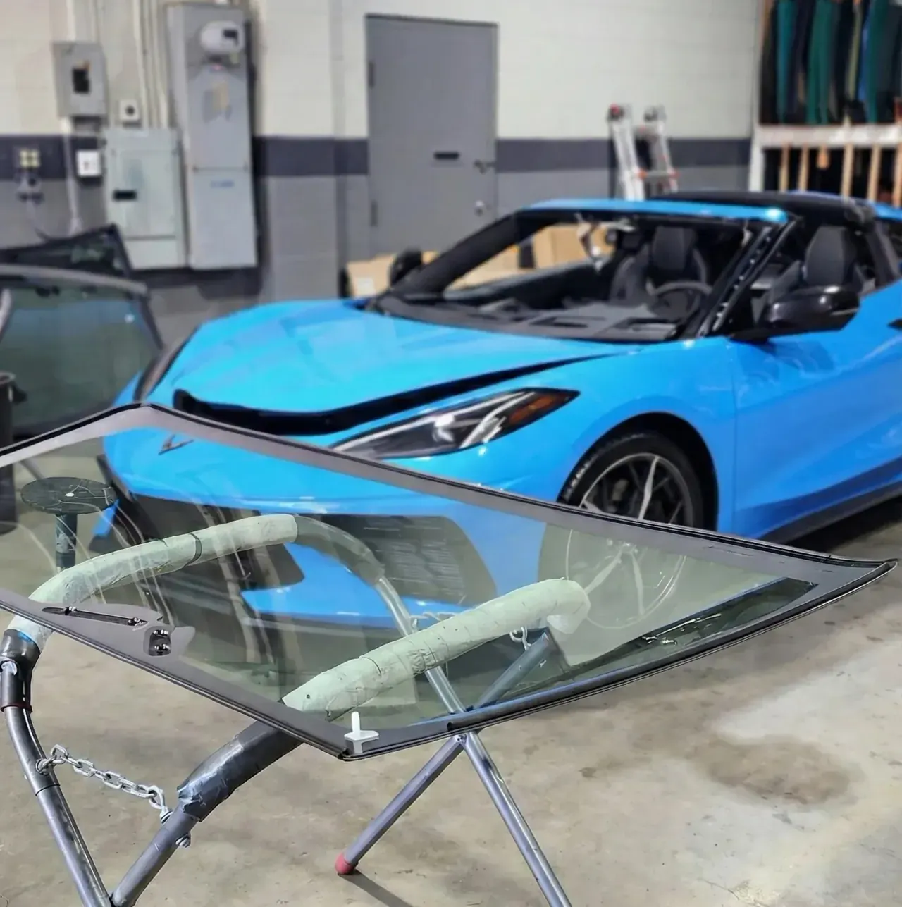 Windshield glass on a padded work stand beside a blue sports car inside the PG Auto Glass shop